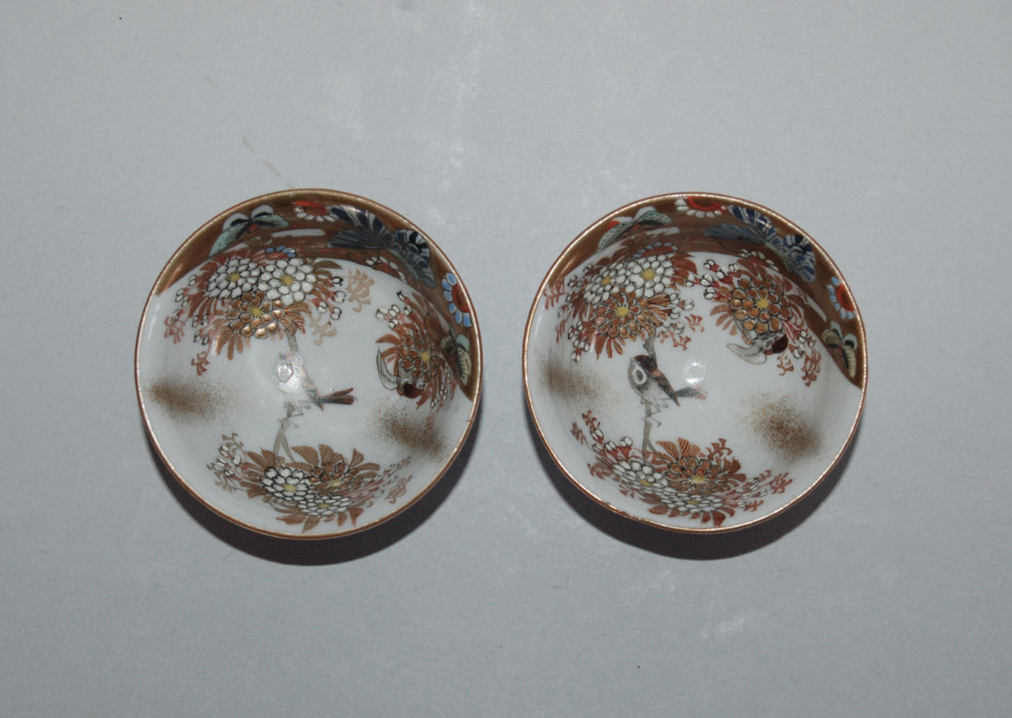 Pair of porcelain sake cups, birds, flowers, butterflies, riverscape, Kutani, Japan