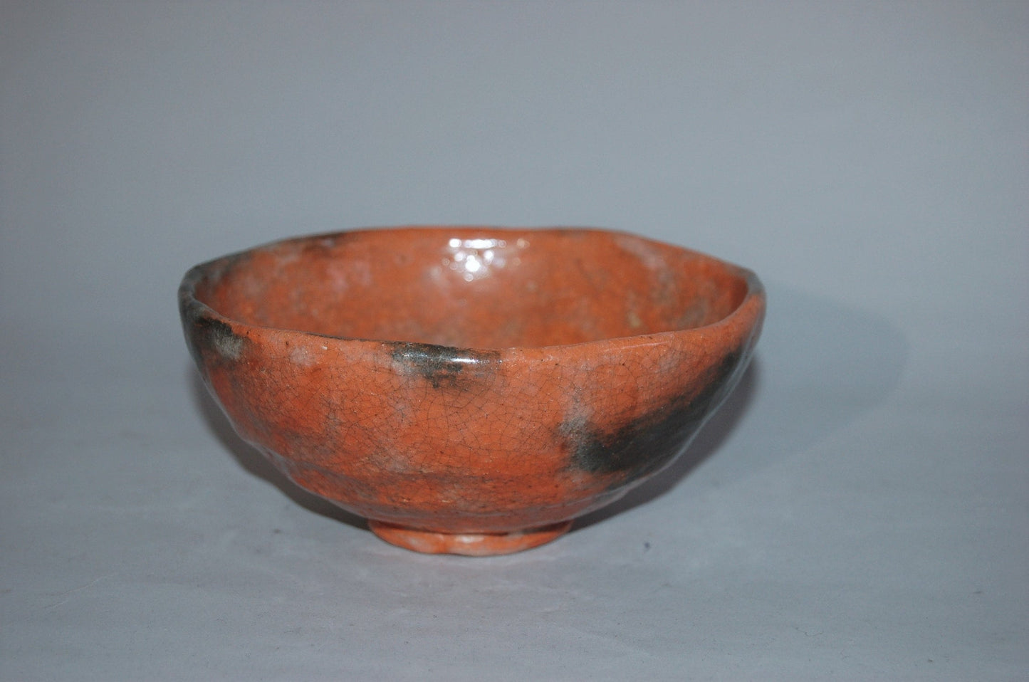 Antique ceramic chawan tea bowl, red Raku ware with black patches, Japan