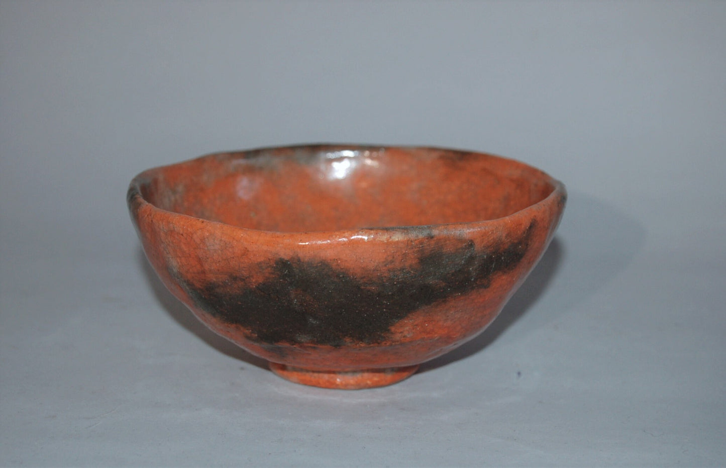 Antique ceramic chawan tea bowl, red Raku ware with black patches, Japan