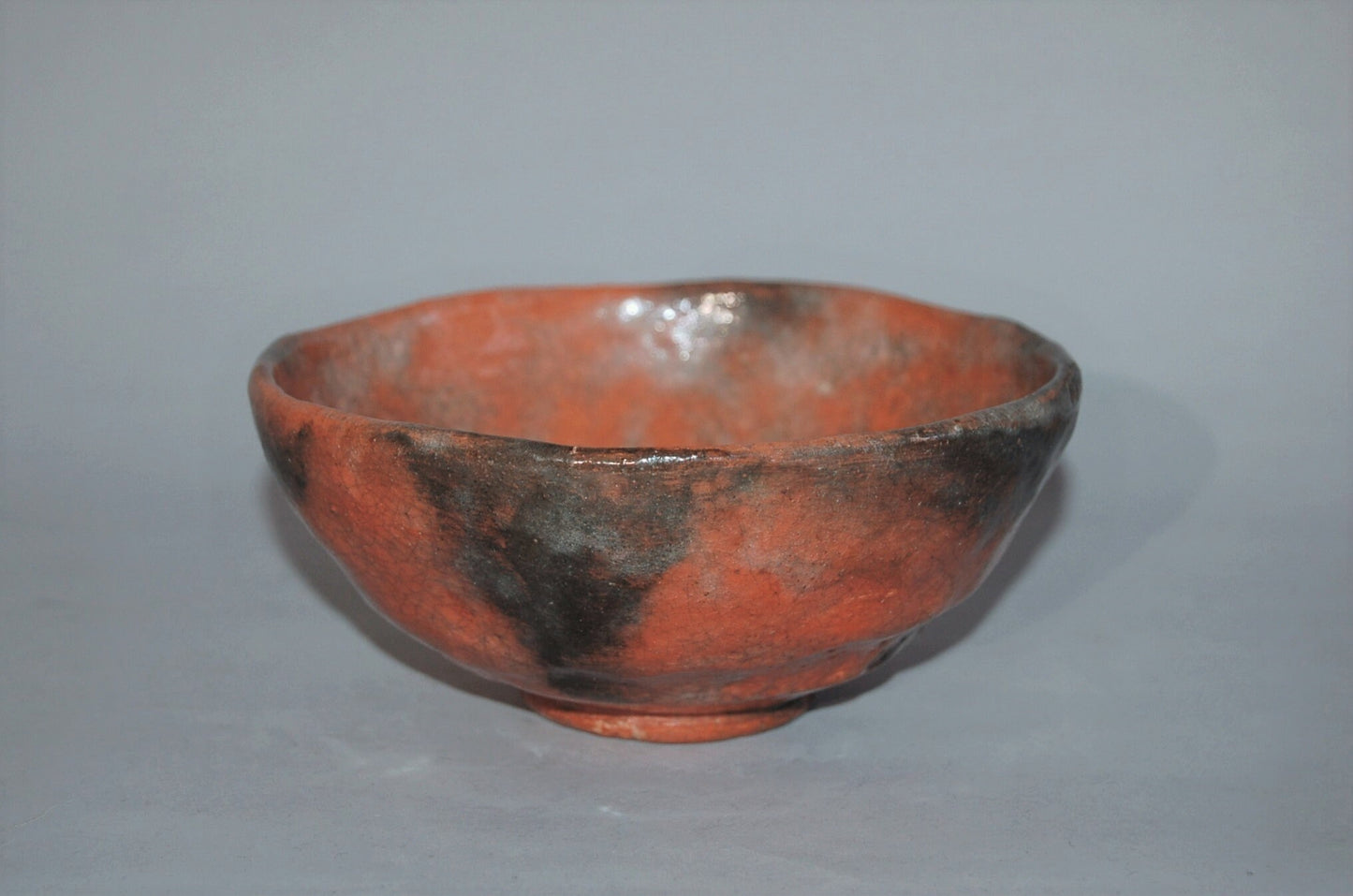 Antique ceramic chawan tea bowl, red Raku ware with black patches, Japan