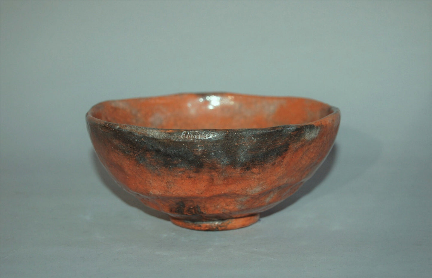 Antique ceramic chawan tea bowl, red Raku ware with black patches, Japan